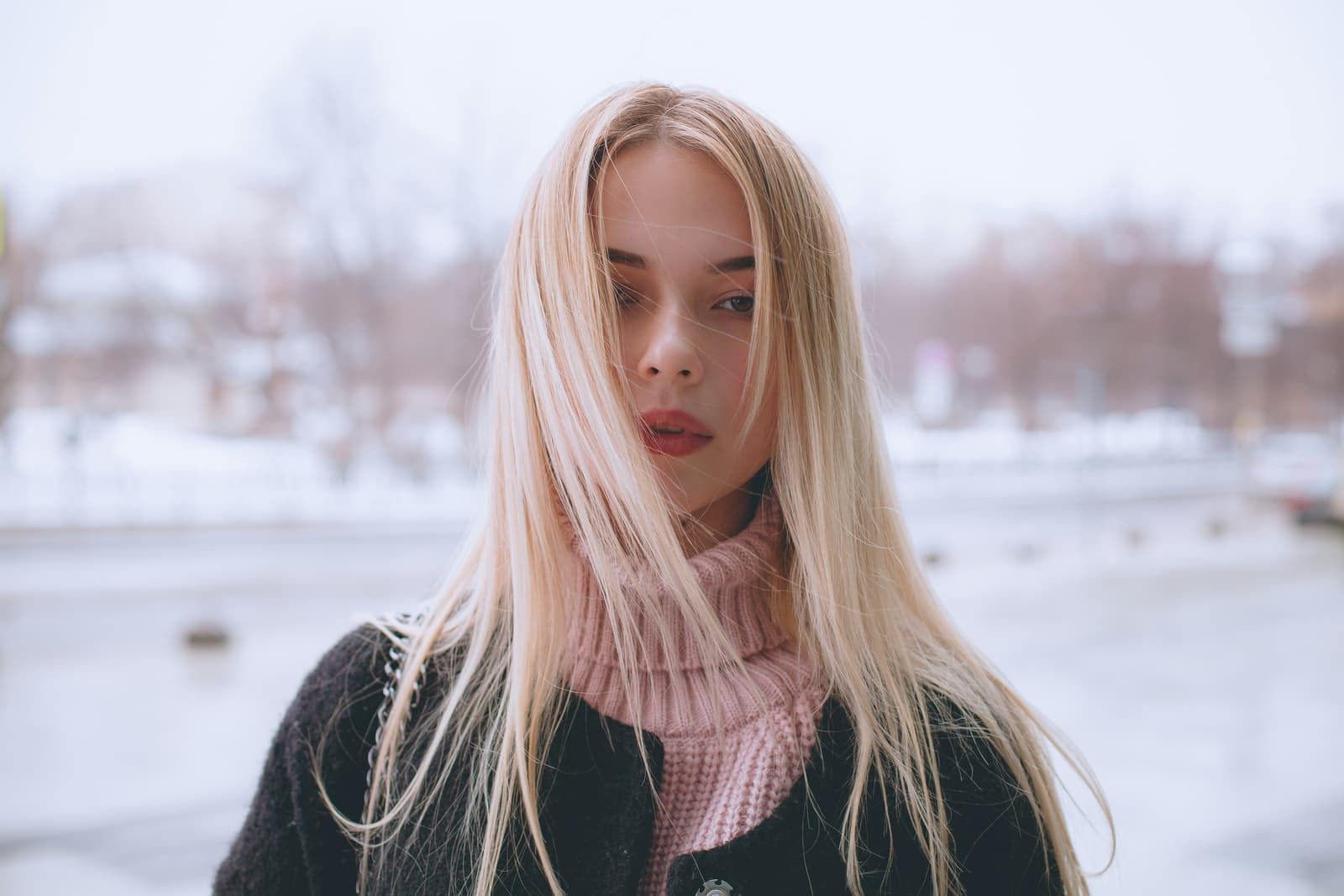 Woman with long, straight blonde hair wearing a winter coat and pink knit scarf
